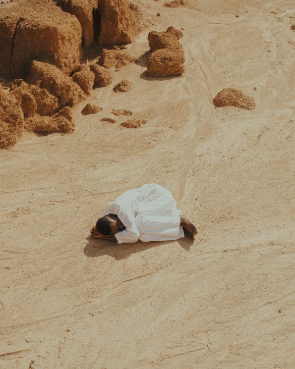 man dressed in white lying curled up on a desert